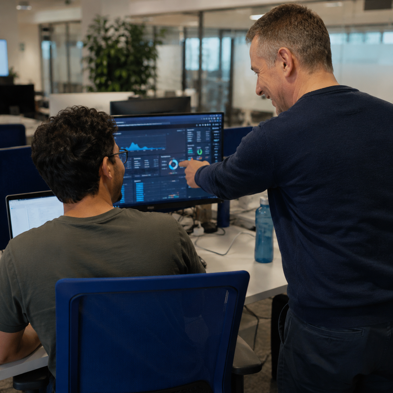 Dos desarrolladores de software analizan datos en una oficina moderna, mostrando un ambiente de trabajo saludable y ergonomía digital promovida por programas de bienestar B2B.